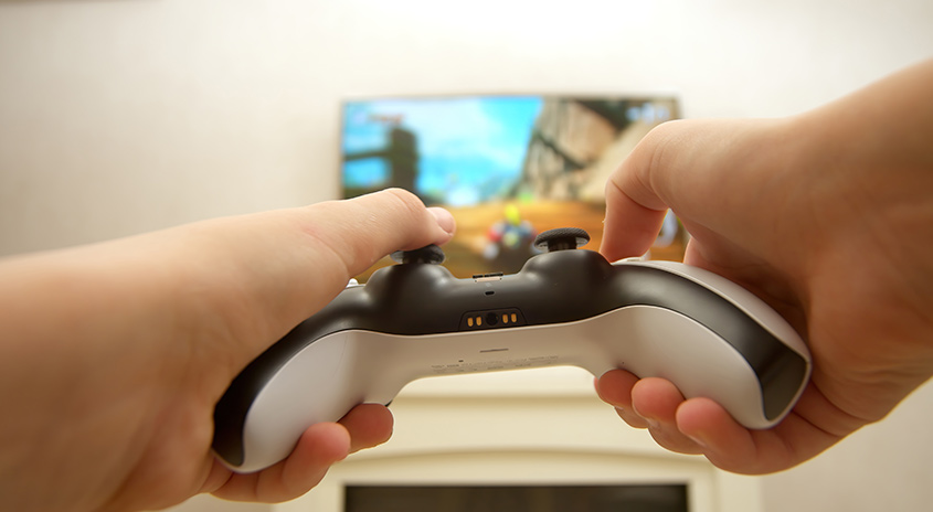 Zwei Hände halten einen weißen und schwarzen Controller vor einem verschwommenen Bildschirm.