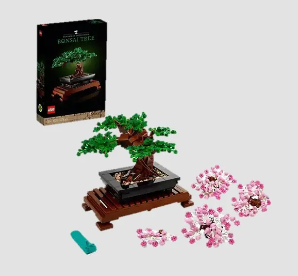 Lego Set eines Bonsai Baums, im Vordergrund liegen kleine rosa Lego Blüten, im Hintergrund steht die Lego Verpackung