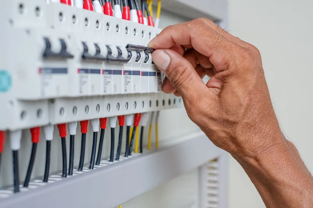 Hand legt einen Schalter an einem Stromkreisverteiler mit mehreren Sicherungen um