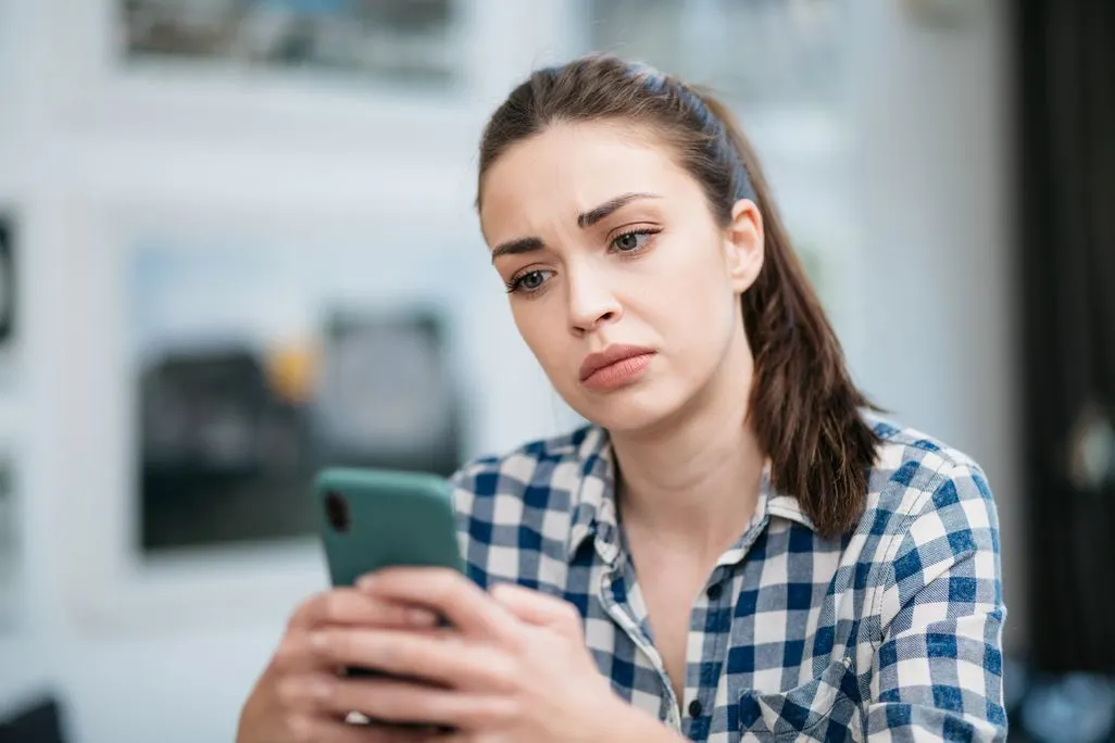 Frau in kariertem Hemd hält Smartphone in beiden Händen.