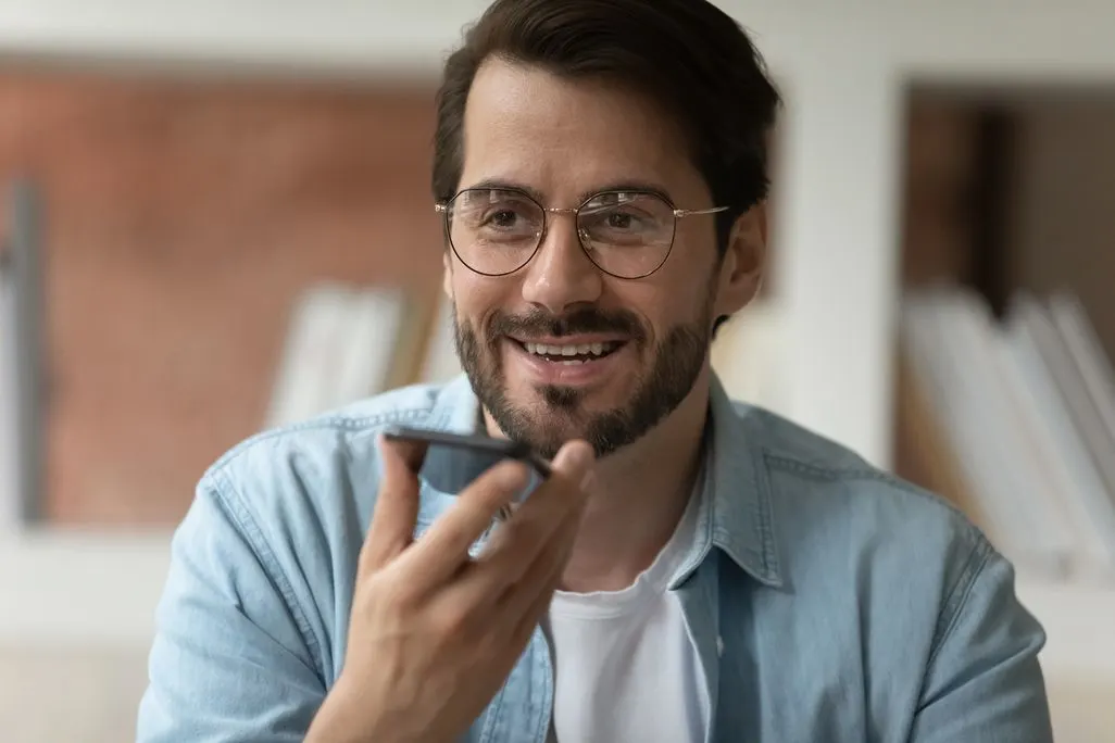 Ein Mann hält ein Smartphone in der Hand und spricht eine Sprachnachricht ein.