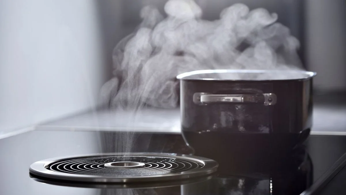 Topf dampft auf dunklem Kochfeld. Ein silberner Dunstabzug saugt daneben den aufsteigenden Dampf ab.