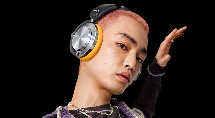 Ein Porträt einer Person mit Kopfhörern mit gelben Polstern und silbernen Lautsprechern auf schwarzem Hintergrund.