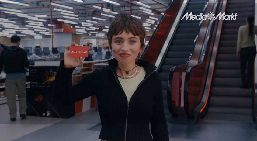 Frau im Markt hält eine MediaMarkt Geschenkkarte in die Höhe und zeigt sie in die Kamera