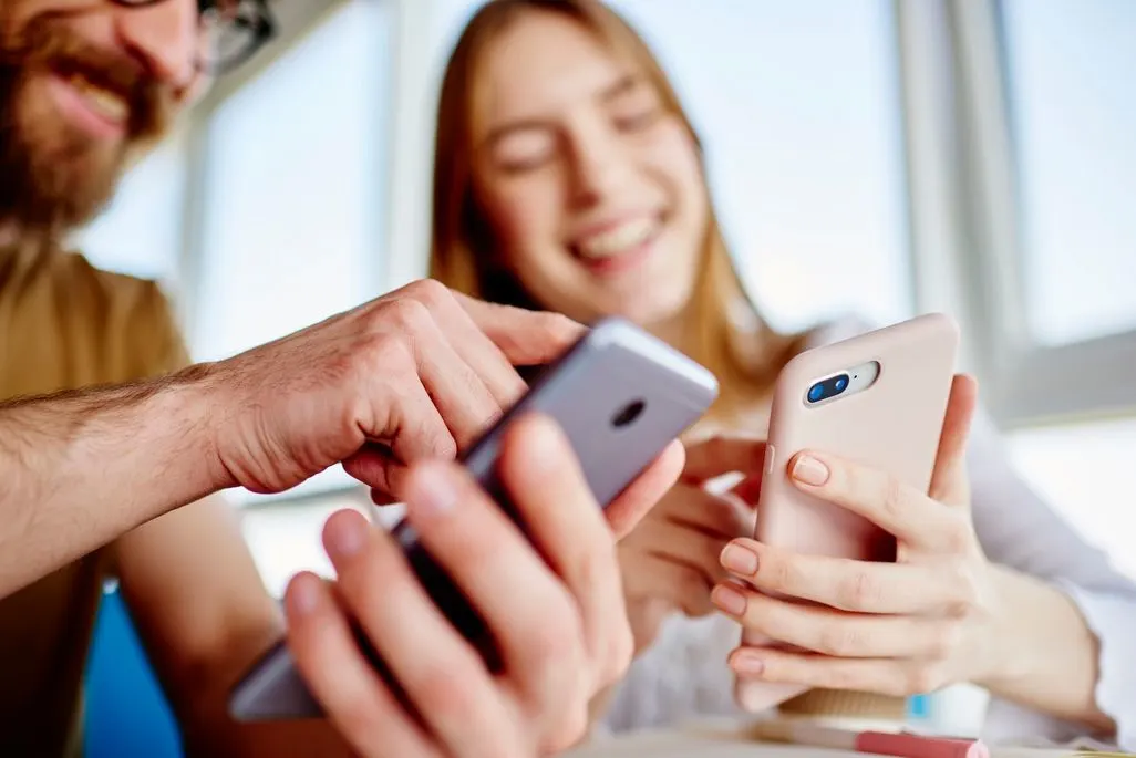 Zwei Personen sitzen zusammen und halten jeweils ein Smartphone in den Händen.