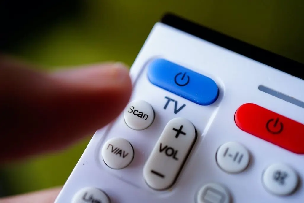 Eine Hand drueckt auf die blaue Einschalttaste einer TV-Fernbedienung