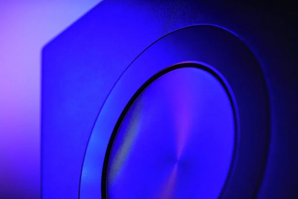 Nahaufnahme eines dunklen, rechteckigen Objekts mit einer runden, gebürsteten Metallscheibe, in blau-violettes Licht getaucht.