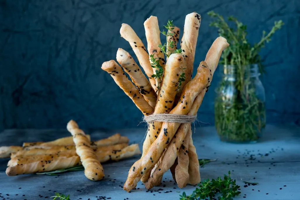 Ein Bündel knuspriger Brotstangen mit Sesam und Kräutern auf einem Tisch.
