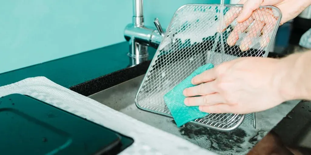 Gitter einer Heissluftfritteuse wird mit einem Schwamm abgewaschen