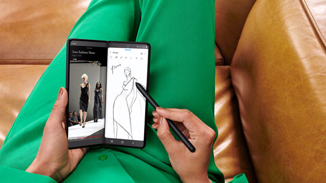 Eine Person in grüner Kleidung hält ein faltbares Telefon und skizziert ein Kleid mit einem Stift.