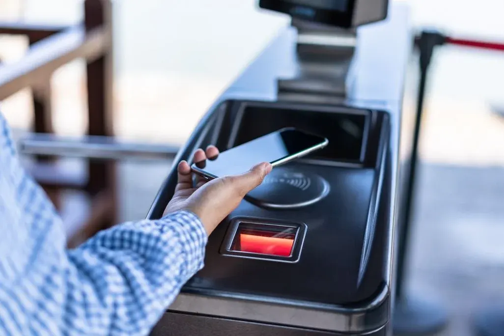 Hand hält schwarzes Smartphone über Terminal mit NFC-Pad und rotem Licht. Person in kariertem Hemd nutzt kontaktlose Bezahlung.