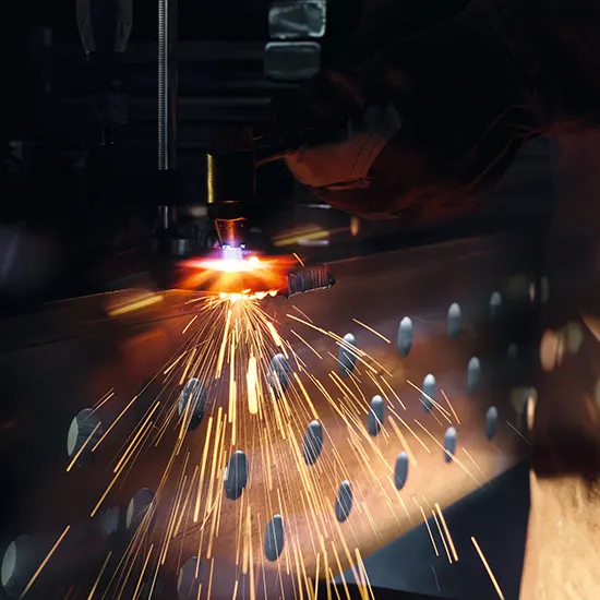 Eine Maschine schneidet Metall mit einem Laser und erzeugt Funken. Das Metall hat ovale Löcher.