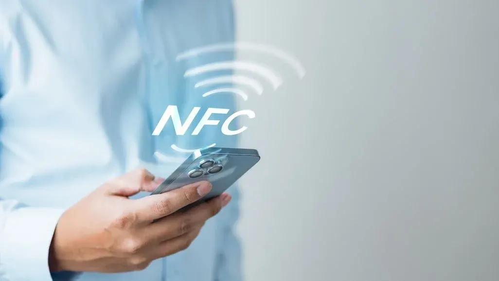 Person hält Smartphone in der Hand, darüber erscheint das NFC-Symbol für kontaktlose Datenübertragung.