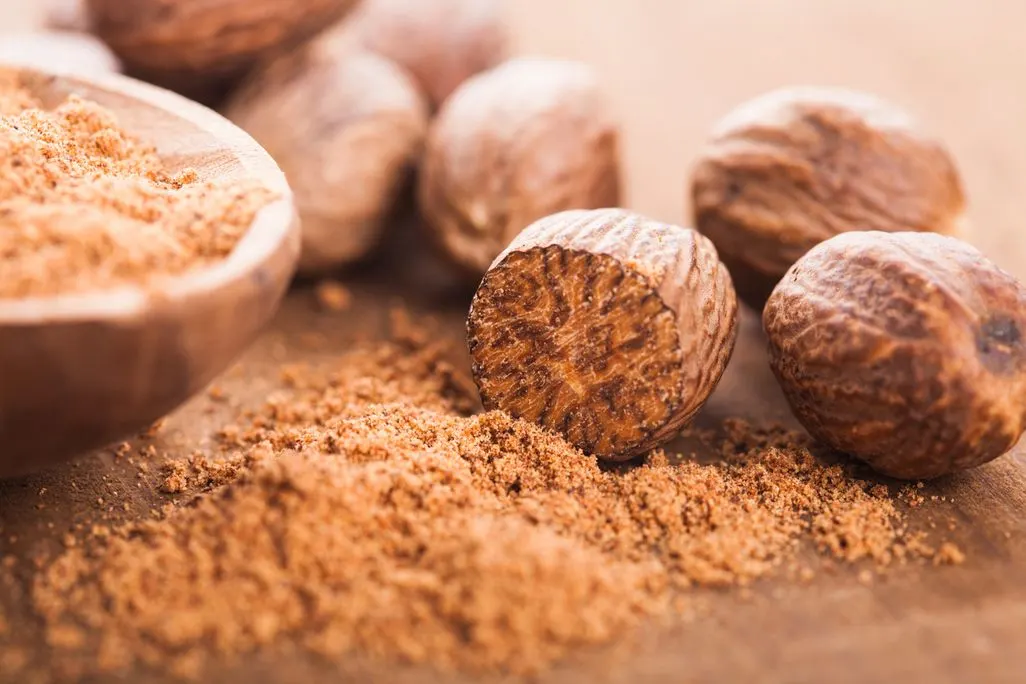 Ganze Muskatnüsse und gemahlene Muskatnuss auf einem Holzbrett.