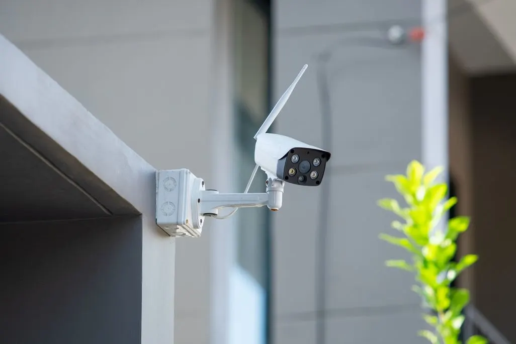 Weisse Ueberwachungskamera mit Antenne ist an einer Hauswand im Aussenbereich montiert