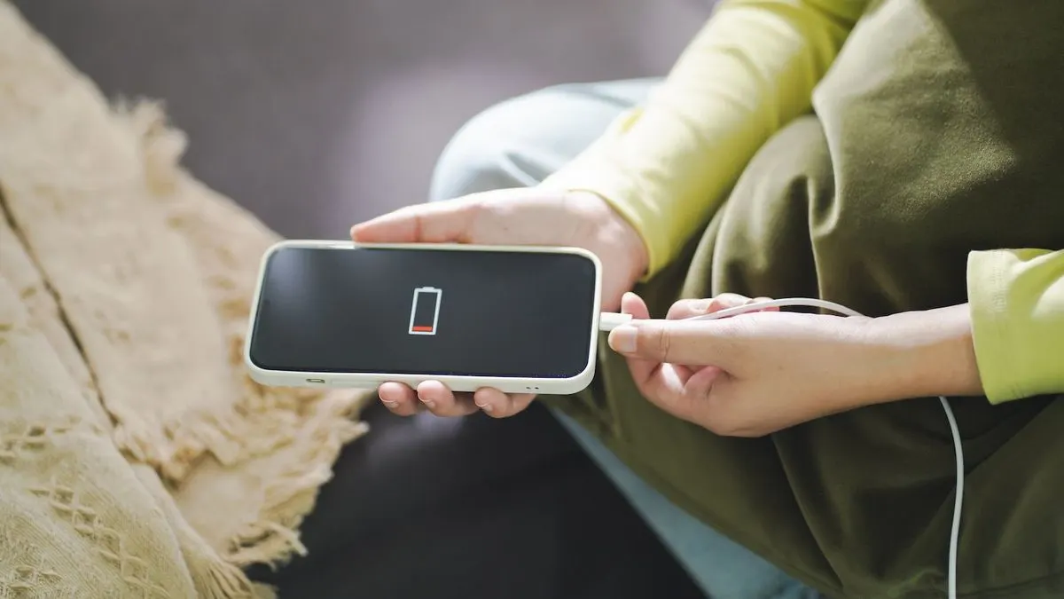Person steckt ein Ladekabel in ein Smartphone mit fast leerem Akku Symbol.