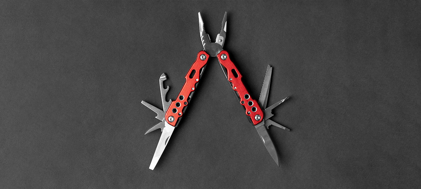 Eine rote Multifunktionszange mit Werkzeugen auf grauem Grund.