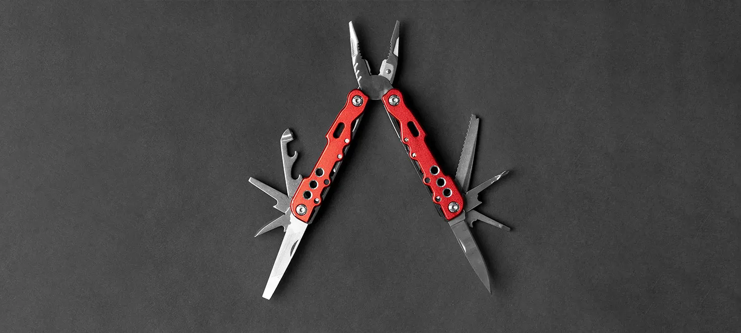 Eine rote Multifunktionszange mit Werkzeugen auf grauem Grund.