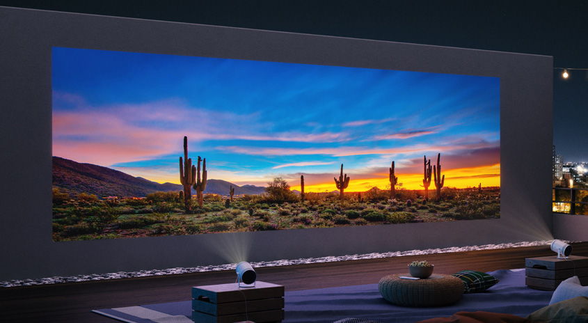 Ein Projektor zeigt eine Wüstenlandschaft mit Kakteen bei Sonnenuntergang. Im Hintergrund ist eine Stadt zu sehen.