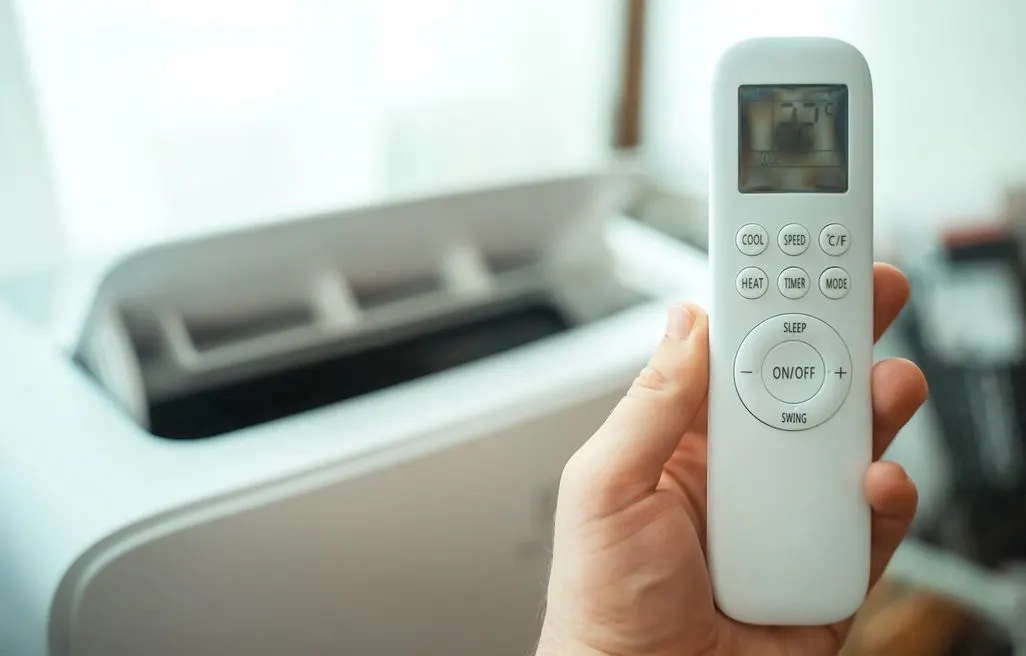Hand haelt Fernbedienung vor ein mobiles Klimageraet