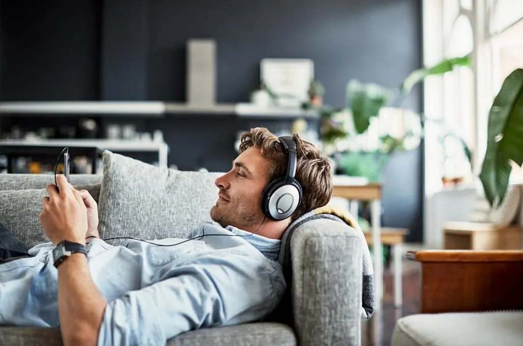 Mann liegt entspannt auf dem Sofa und hört Musik mit großen Kopfhörern.