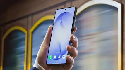Hand mit modernem Smartphone mit nahezu randlosem Display, das vor einem bunten, vorbeirauschenden Hintergrund in die Höhe gehalten wird.