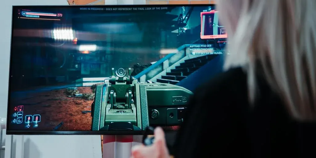 Person spielt einen Ego-Shooter: Auf dem Monitor ist die Waffe im Visier zu sehen, im Vordergrund hält die Person einen Controller.