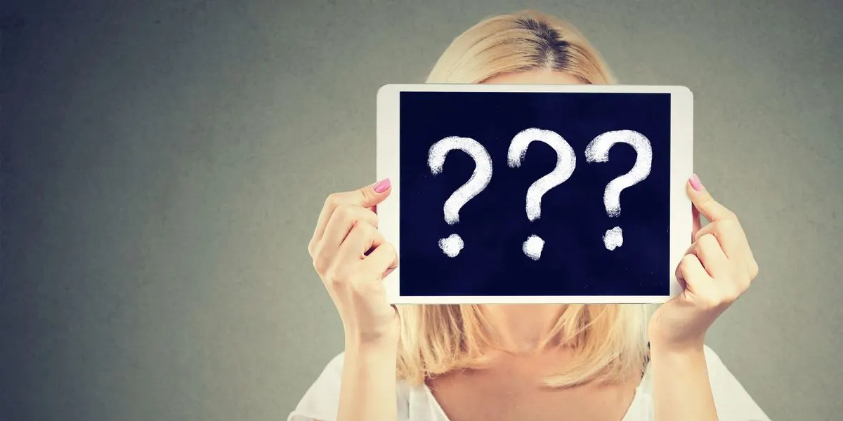 Frau mit blonden Haaren haelt ein Tablet mit drei grossen Fragezeichen vor ihr Gesicht