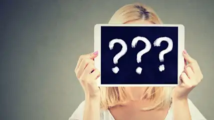 Frau mit blonden Haaren haelt ein Tablet mit drei grossen Fragezeichen vor ihr Gesicht