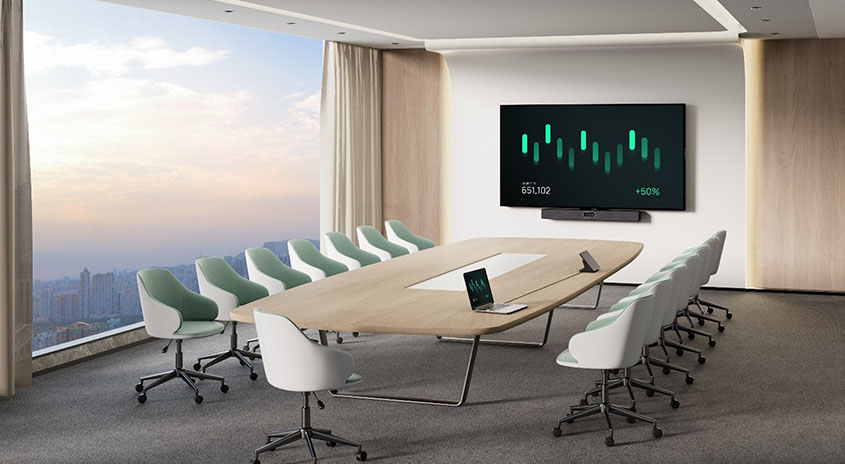 Heller, moderner Konferenzraum: ein langes, ovales Holztisch-Set mit eingelassener Kabelöffnung, zwölf weiße Bürodrehstühle mit mintgrünen Polstern auf Rollen, ein geöffnetes Laptop und ein Tablet auf dem Tisch, grauer Teppich, helle Holzpaneele an der Wand, großes Panoramafenster mit Blick auf eine Stadt bei Sonnenuntergang und ein an der Wand montierter Bildschirm, der ein grünes Balkendiagramm anzeigt.