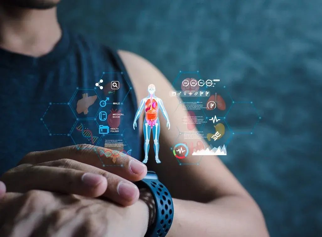 Arm mit dunkelblauer Smartwatch zeigt Hologramm eines menschlichen Körpers mit Organen, umgeben von medizinischen Daten und Symbolen auf dunklem Hintergrund.