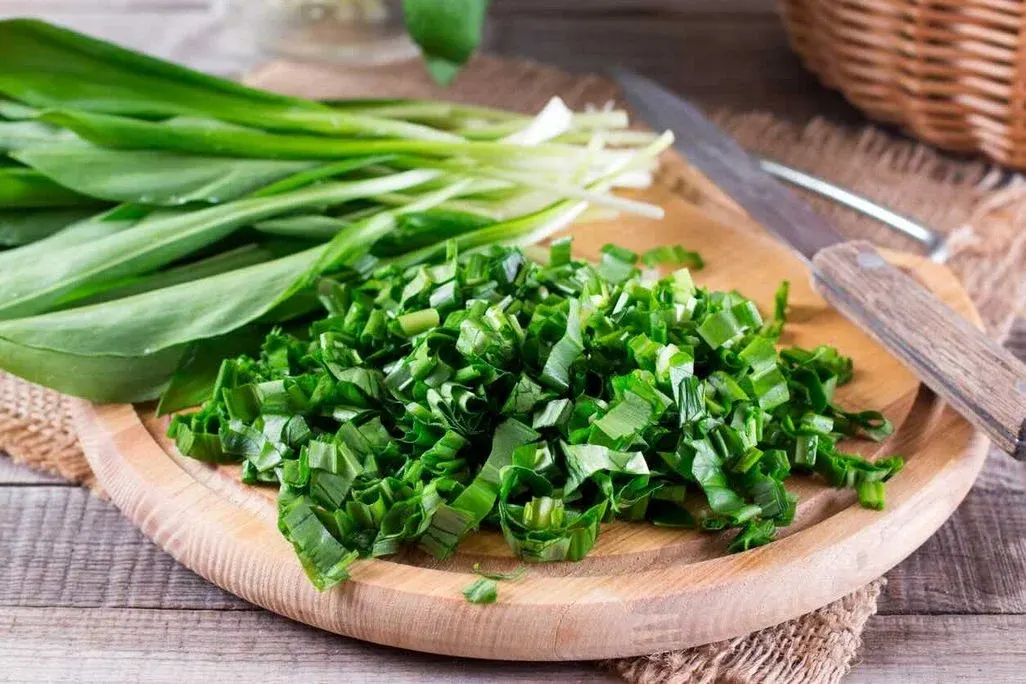 Holzbrett mit frisch geschnittenem Bärlauch, daneben ganze Blätter und ein Messer – vorbereitet zum Kochen in der Küche.