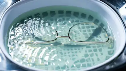 Brille in bewegtem Wasser eines Ultraschallreinigers, mit Gittermuster am Boden.