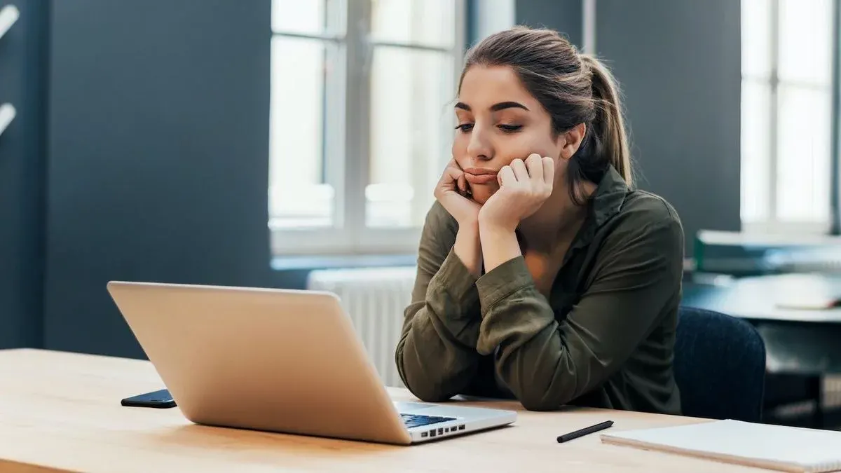 Frau schaut nachdenklich auf den Screen eines Laptops am Schreibtisch.