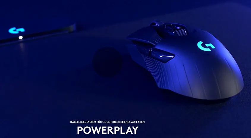 Eine blaue Gaming-Maus mit leuchtendem "G"-Logo liegt auf einer dunklen Oberfläche neben einem Gerät mit einem weiteren "G"-Logo.