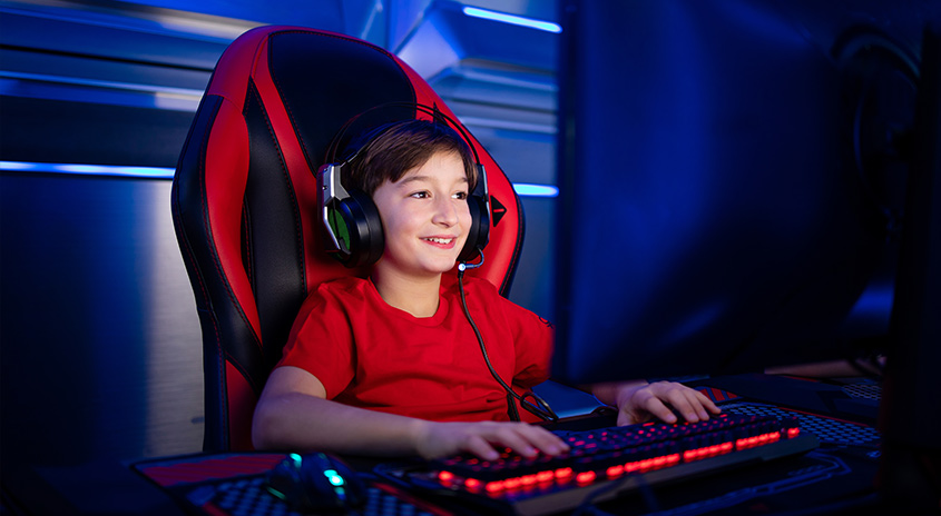 Ein roter Gaming-Stuhl steht vor einem leuchtenden, roten Keyboard auf einem Tisch in einem dunklen Raum.