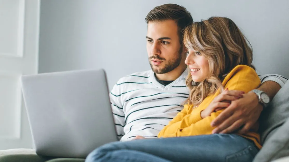 Ein Paar sitzt auf dem Sofa und schaut gemeinsam auf einen Laptop.
