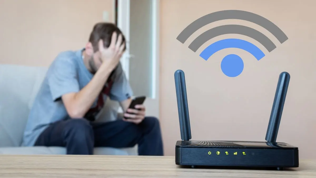 Verzweifelter Mann sitzt mit Smartphone auf dem Sofa hinter einem WLAN-Router, darüber ist ein großes WLAN-Symbol eingeblendet.