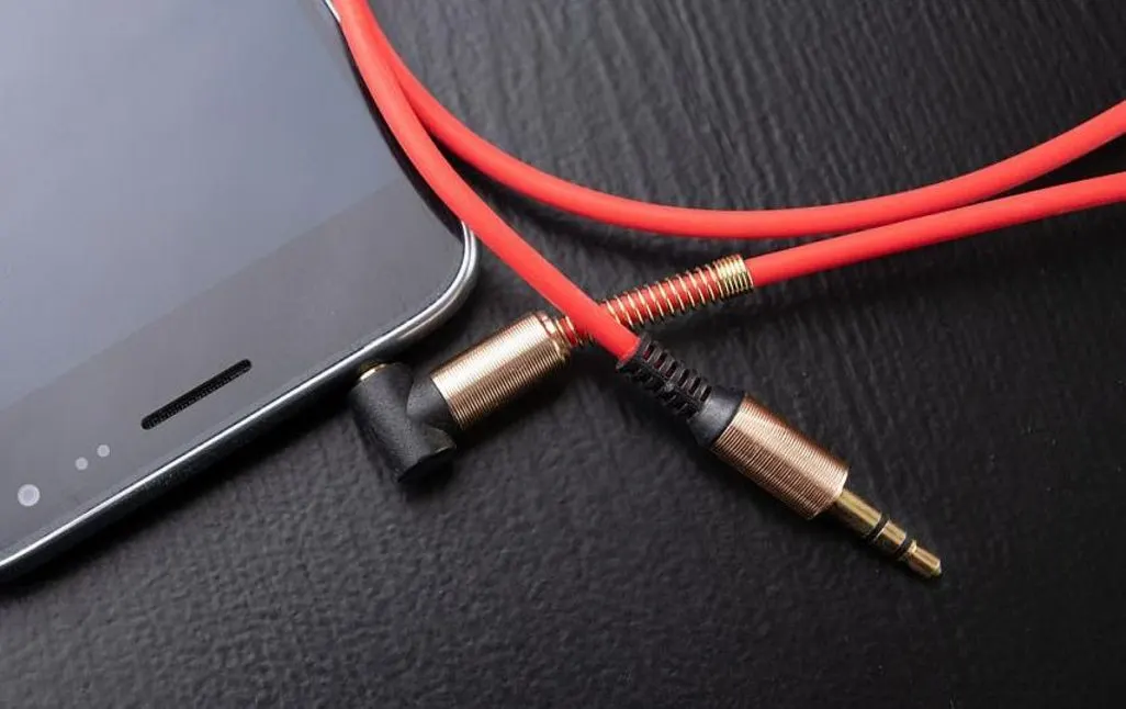 Rotes Audiokabel mit Klinkenstecker liegt neben einem Smartphone auf schwarzem Tisch.