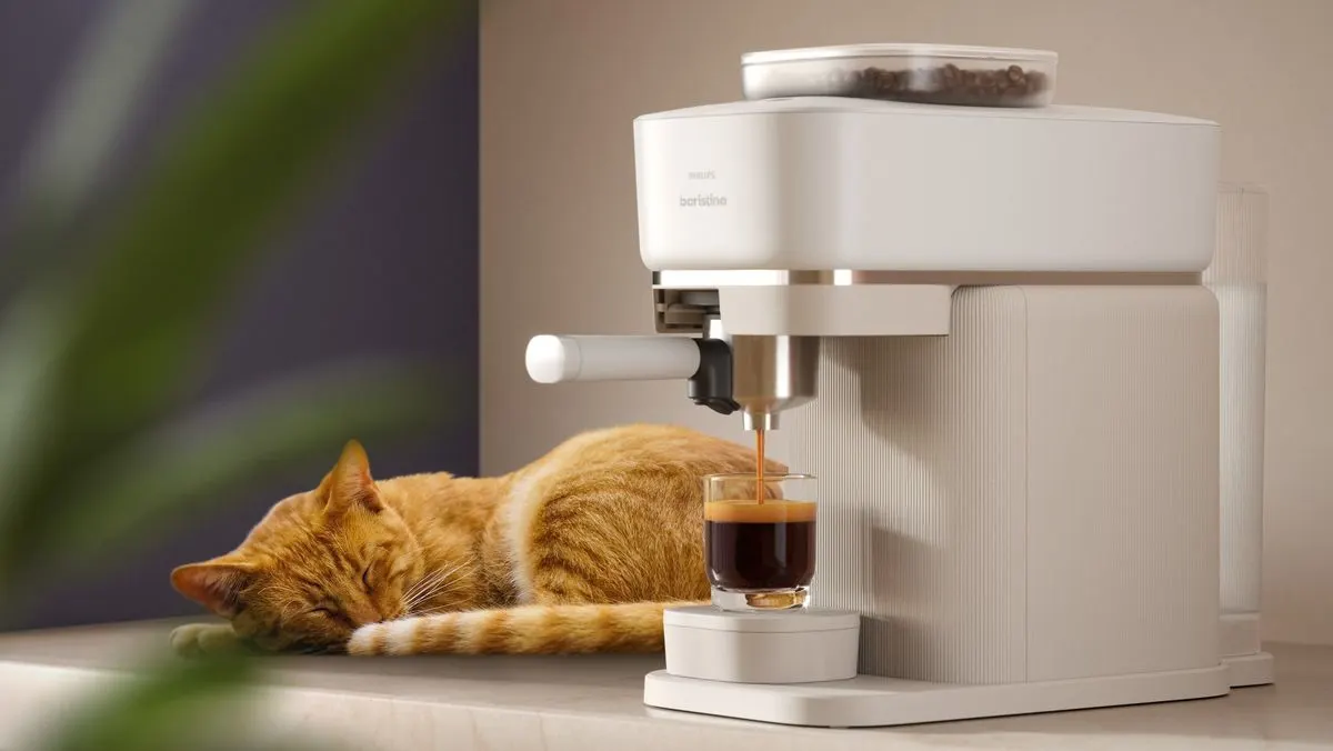 Orange Katze schläft neben weißer Philips Baristina Kaffeemaschine, die Espresso in Glas füllt. Bohnen oben sichtbar.