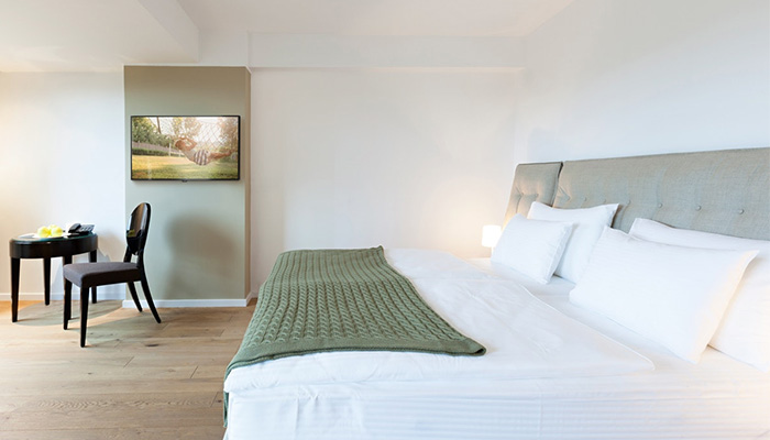 Ein Hotelzimmer mit einem Bett, einem Nachttisch und einem Stuhl. Ein Fernseher hängt an der Wand.
