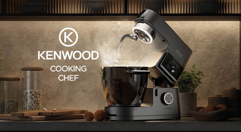 Kenwood Cooking Chef Küchenmaschine auf einer Arbeitsplatte, dampfende Schüssel, modernes Design, im Hintergrund Zutaten und Kenwood-Logo.