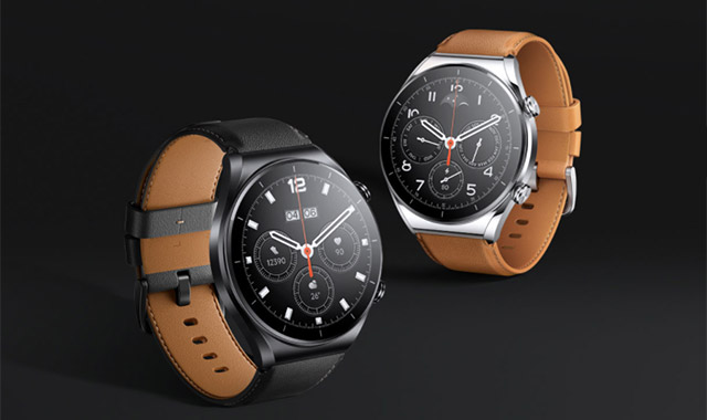 Zwei Smartwatches mit schwarzem Zifferblatt und Lederarmband vor schwarzem Hintergrund. Eine hat ein silbernes Gehäuse.