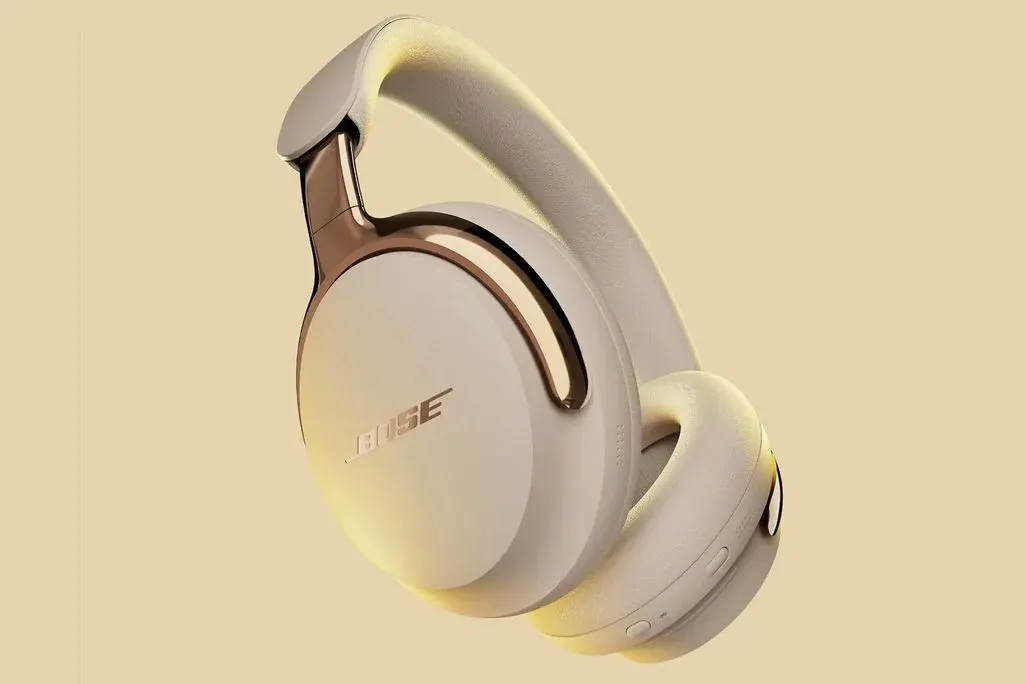 Weiße Bose-Over-Ear-Kopfhörer mit rosegoldenen Metallelementen auf beigem Hintergrund in Three-Quarter-Ansicht, die das moderne Design mit Ohrmuschel und Kopfband zeigt.
