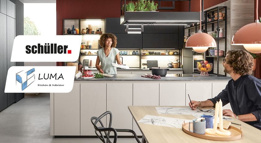 Eine Küche mit einer Frau, die kocht, und einem Mann, der an einem Tisch mit Kerzen und Zeichnungen sitzt. Logos von Schüller und Luma.