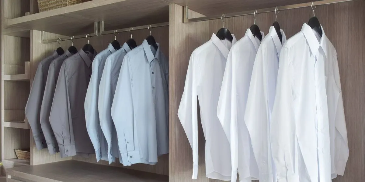 Gebügelte weiße, hellblaue und graue Hemden hängen in einem Schrank.