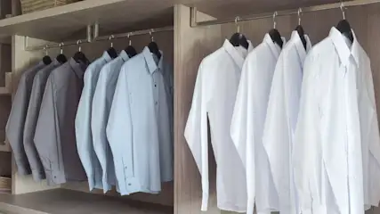 Gebügelte weiße, hellblaue und graue Hemden hängen in einem Schrank.