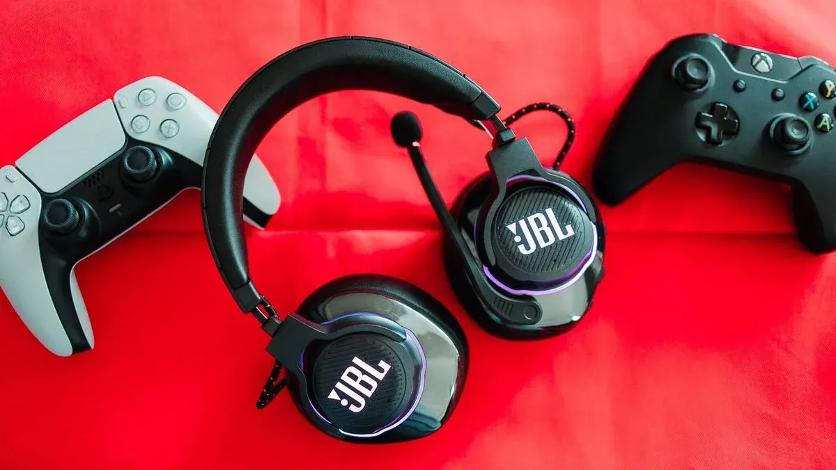 PS5 Controller, JBL-Headset und Xbox Controller liegen nebeneinander auf rotem Untergrund.