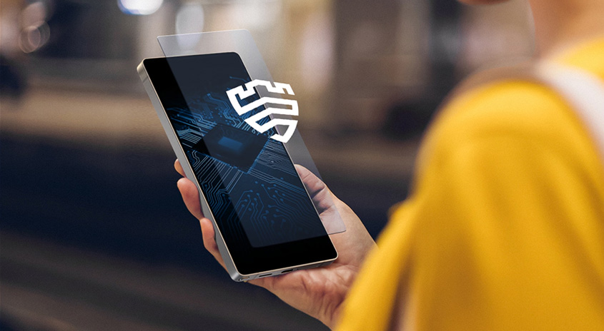 Ein silbernes Smartphone mit einem weißen Sicherheitsschild-Symbol wird von einer Hand gehalten.