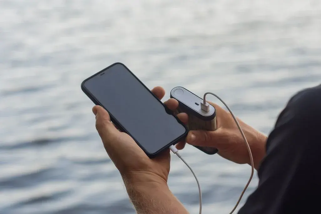 "Person hält ein Smartphone in der Hand und verbindet es mit kabellosen Kopfhörern am Strand oder See